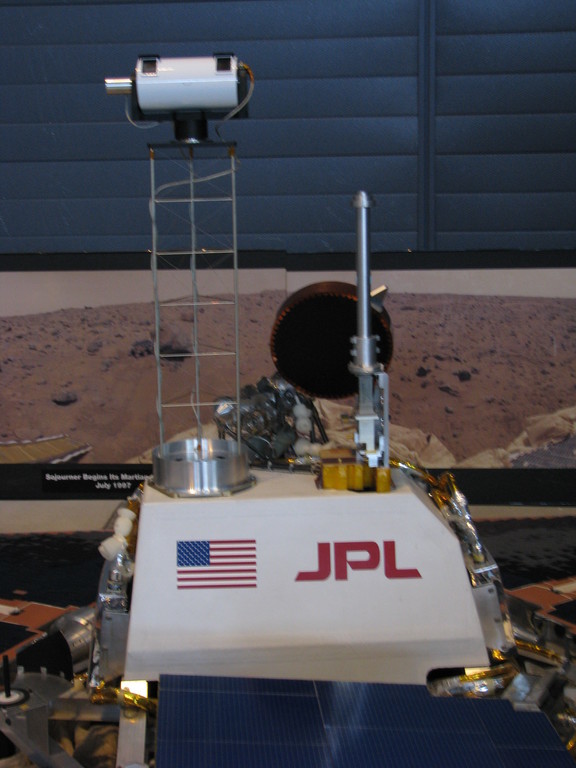 A view of the top of Pathfinder's mast with Imager for Mars Pathfinder (IMP), its only camera. The high gain (flat and round) and omnidirectional (thin vertical cylinder) antennas at visible just right of the center towards the bottom.